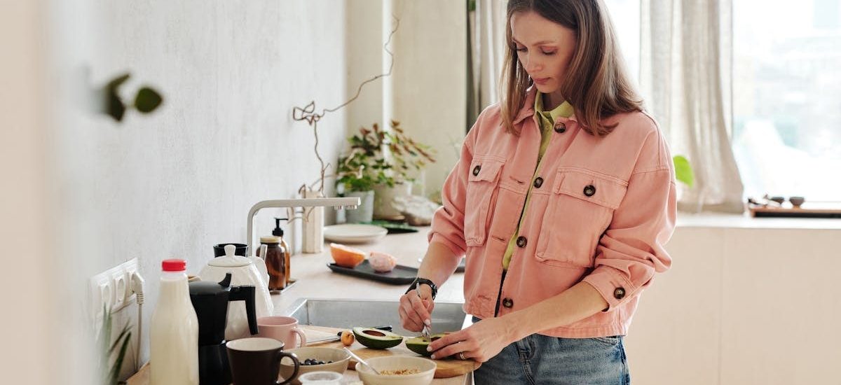 A woman slices an avocado in a bright, modern kitchen with natural light.
