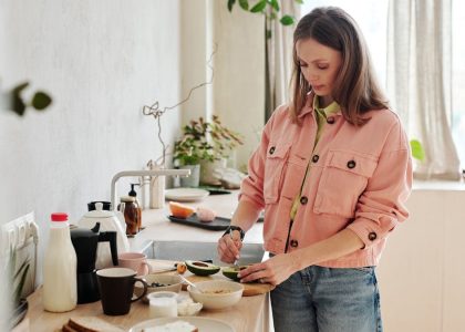 A woman slices an avocado in a bright, modern kitchen with natural light.