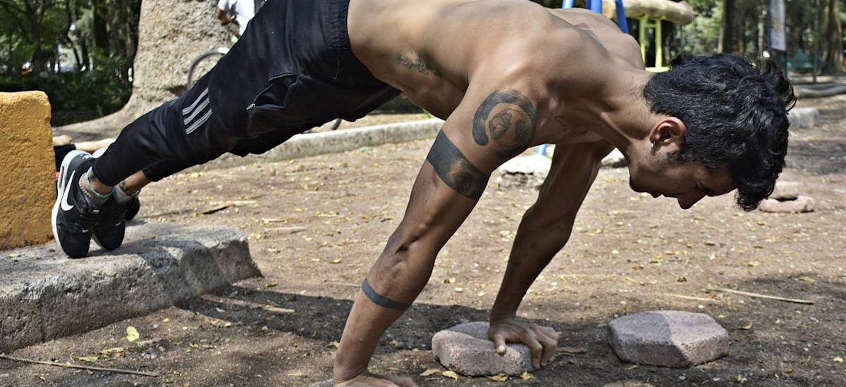 Athletic man performing elevated push-ups on rocks in a park setting.